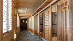 Un pasillo con suelo de esteras de tatami, puertas correderas de madera y un letrero que indica un baño.