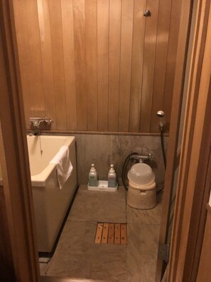 Een kleine badkamer met houten lambrisering, een bad, toilet en handzeepdispensers op de vloer.