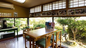 Una habitación con una mesa y sillas de madera, una cafetera y un ventanal con vistas a zonas verdes.