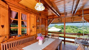 A wooden cabin with a dining area, large windows, and a view of the landscape.