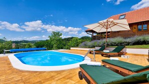 A wooden deck with a swimming pool, lounge chairs, and a wooden house with a red roof.