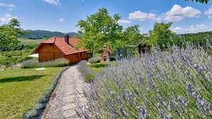 A rustic wooden cabin with a red-tiled roof, surrounded by a lavender field and a stone pathway.
