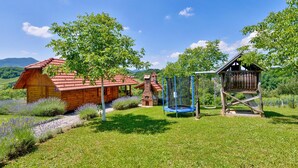 A rustic wooden cabin with a red roof, surrounded by lush greenery and a clear blue sky.