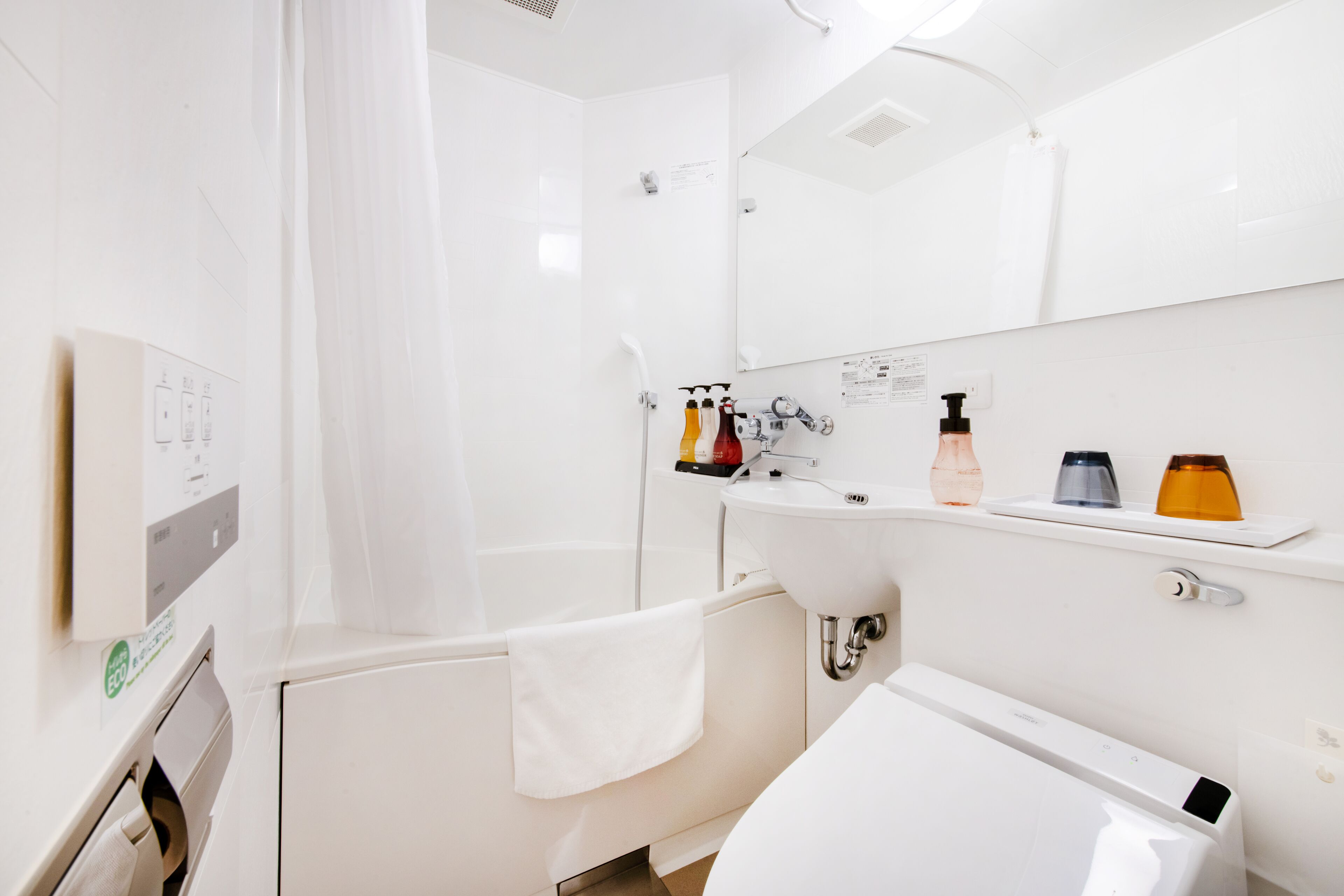 A modern bathroom with a bathtub, a sink, and a mirror. There are toiletries on the sink and a towel hanging on the wall.