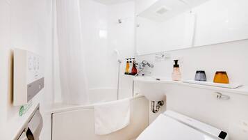A modern bathroom with a bathtub, a sink, and a mirror. There are toiletries on the sink and a towel hanging on the wall.