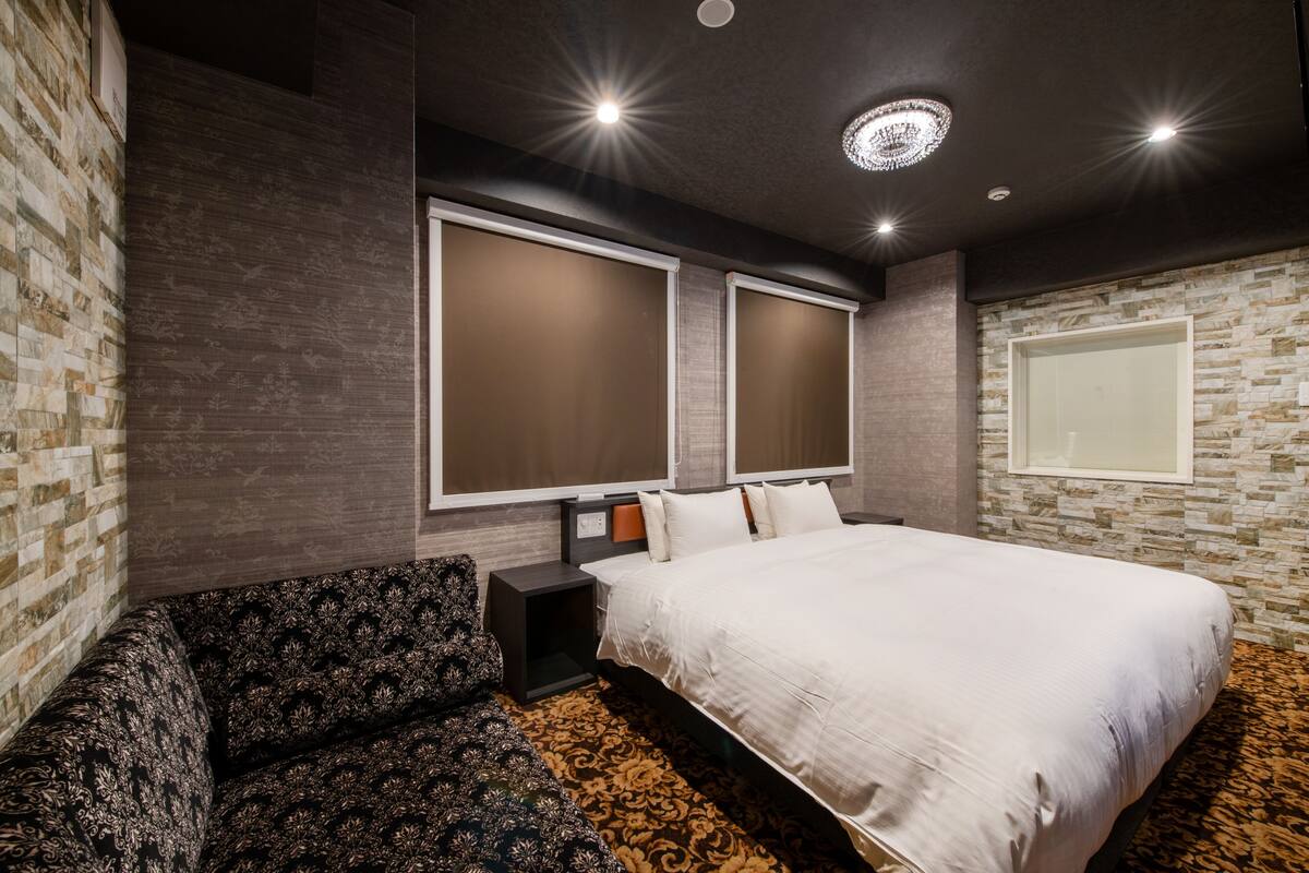 A modern hotel room with a large bed, a sofa, and a large window.