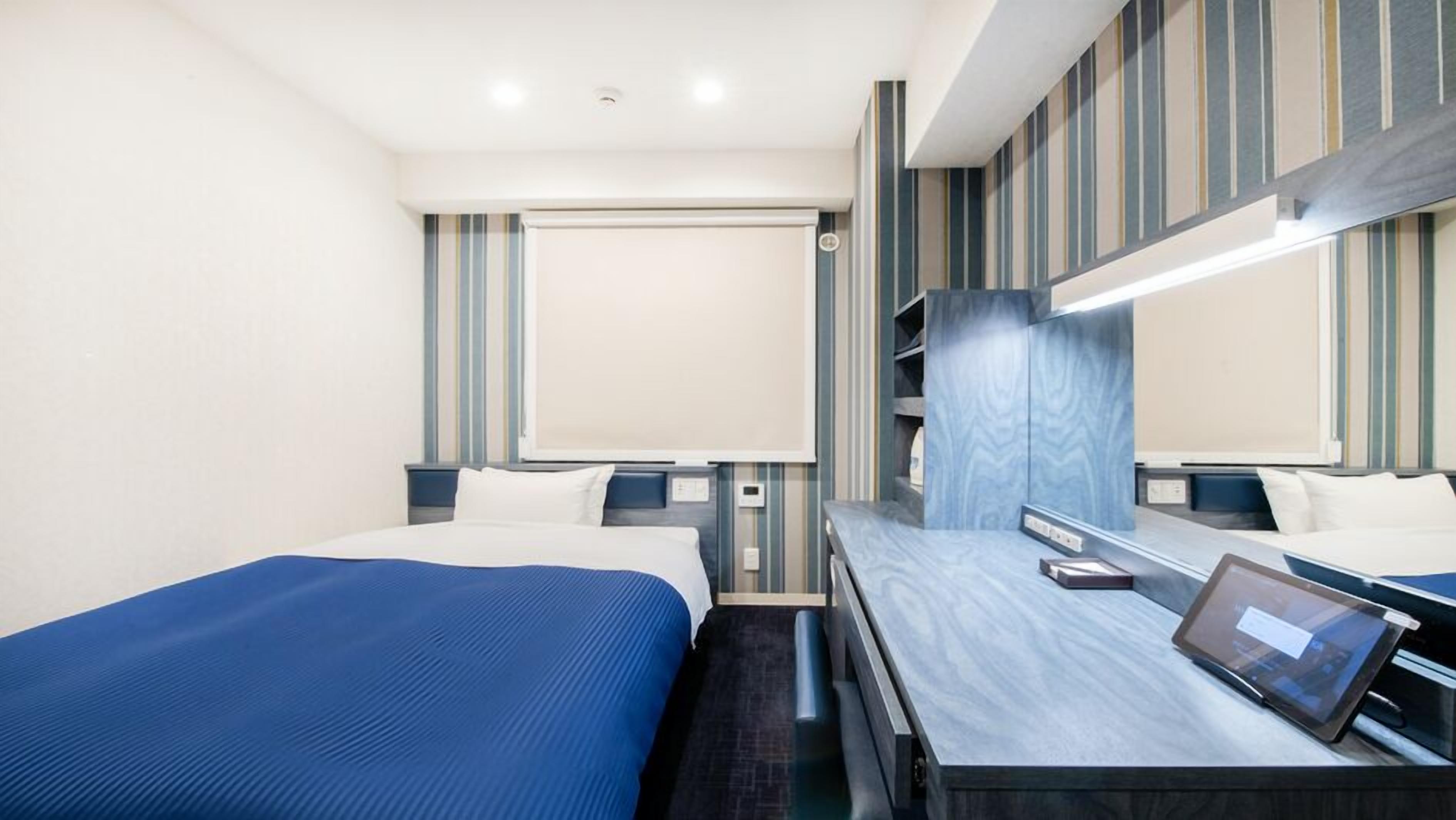 Quarto de hotel com duas camas, um espelho grande, uma escrivaninha com um tablet e decoração de parede listrada.