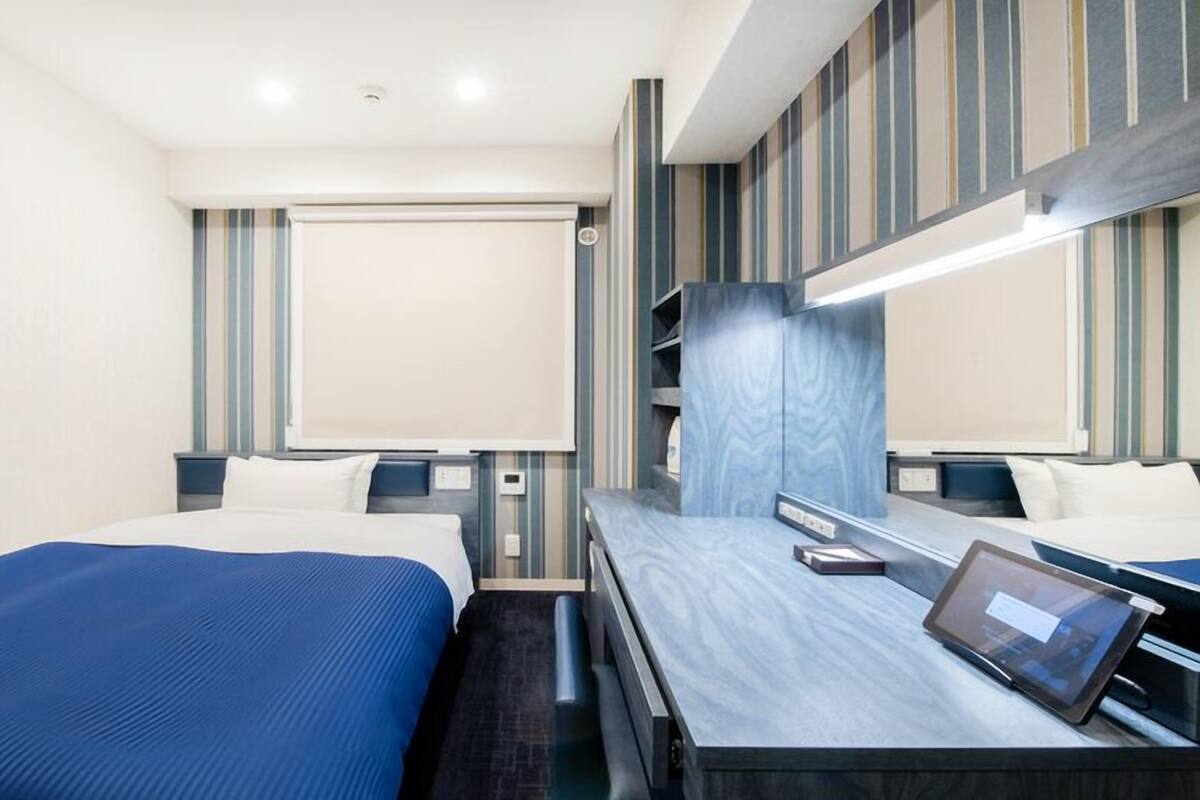 A hotel room with two beds, a large mirror, a desk with a tablet, and striped wall decor.