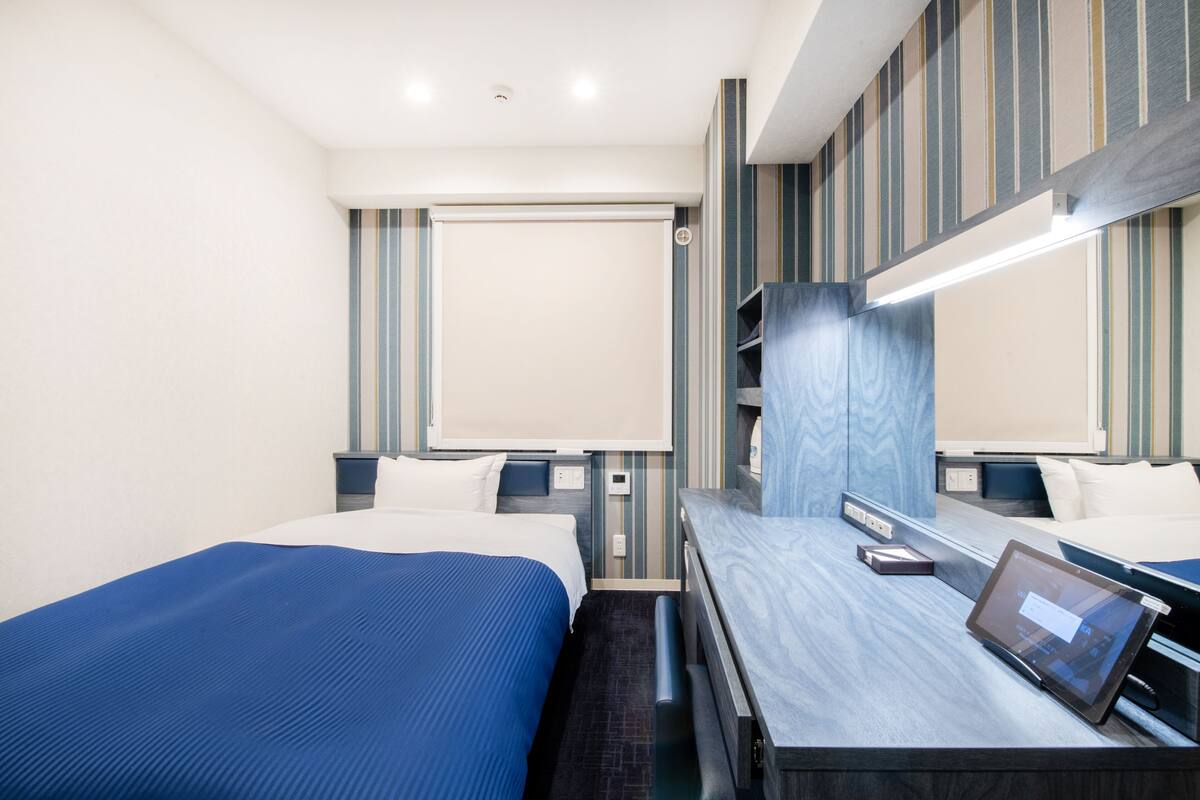 A modern hotel room with a large bed, a desk with a tablet, and a large mirror.