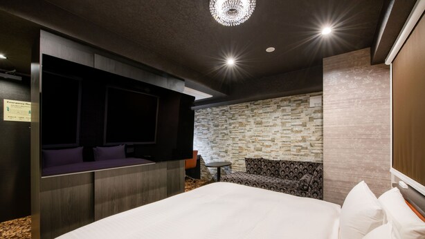 Une chambre d’hôtel avec un grand lit, un coin salon équipé d’une télévision et un mur décoré d’un motif imitant la pierre.