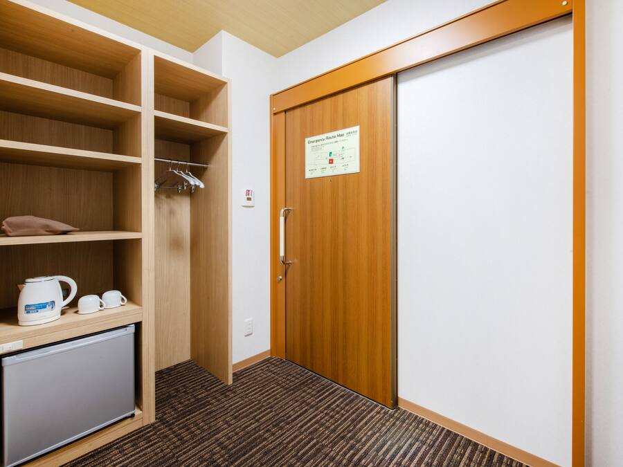 A hotel room with a wooden wardrobe, a small fridge, and a coffee maker.