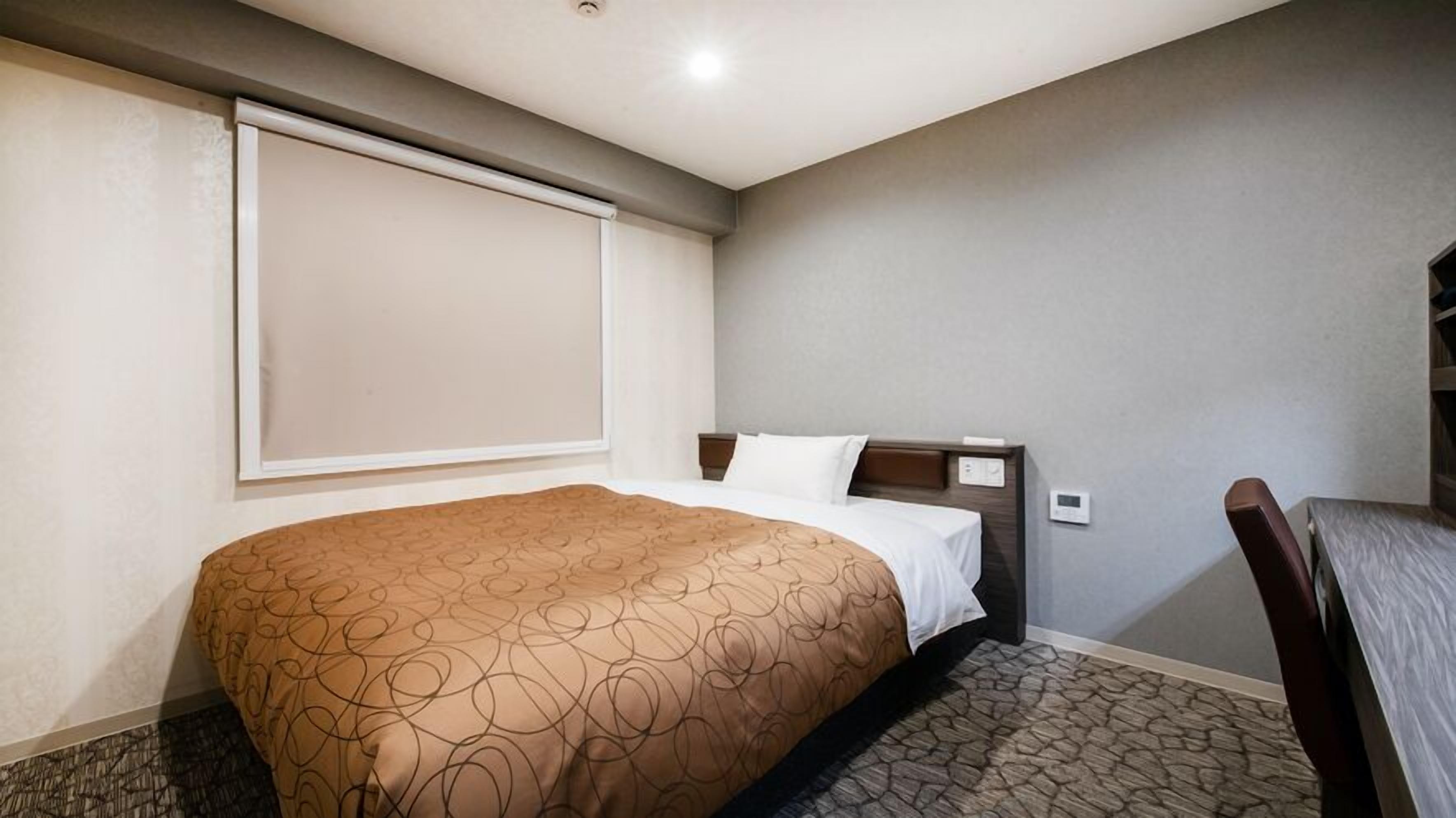 Quarto de hotel com cama, cabeceira, janela e uma cadeira.