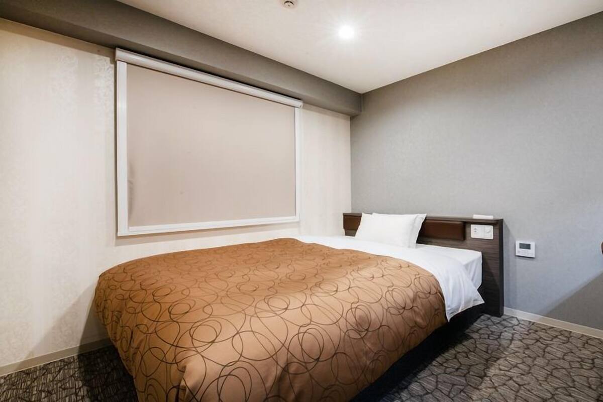 A hotel room with a bed, a headboard, a window, and a chair.