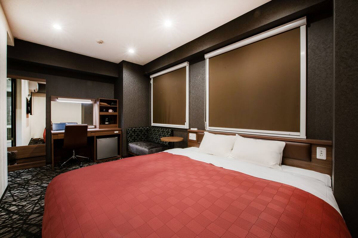 A hotel room with a large bed, a desk with a chair, a small table, and a mirror.