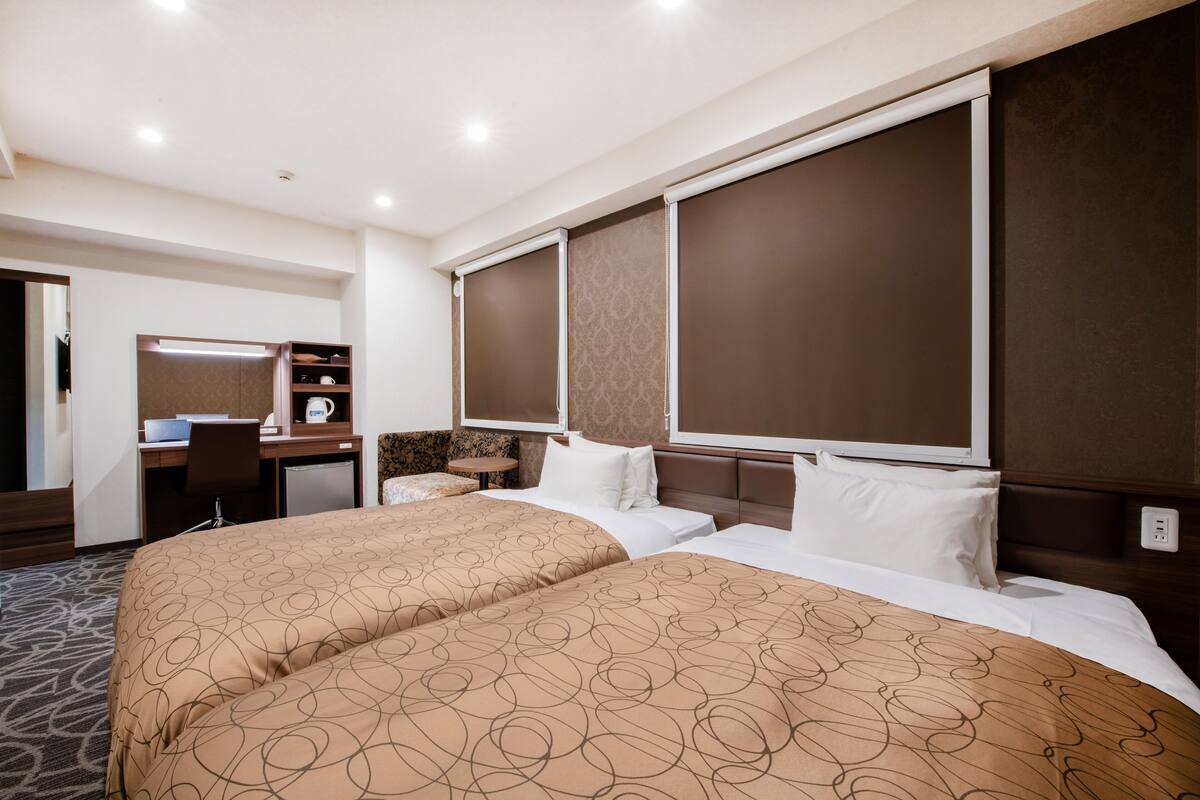 A hotel room with two beds, a desk, a chair, a small table, and a mirror.