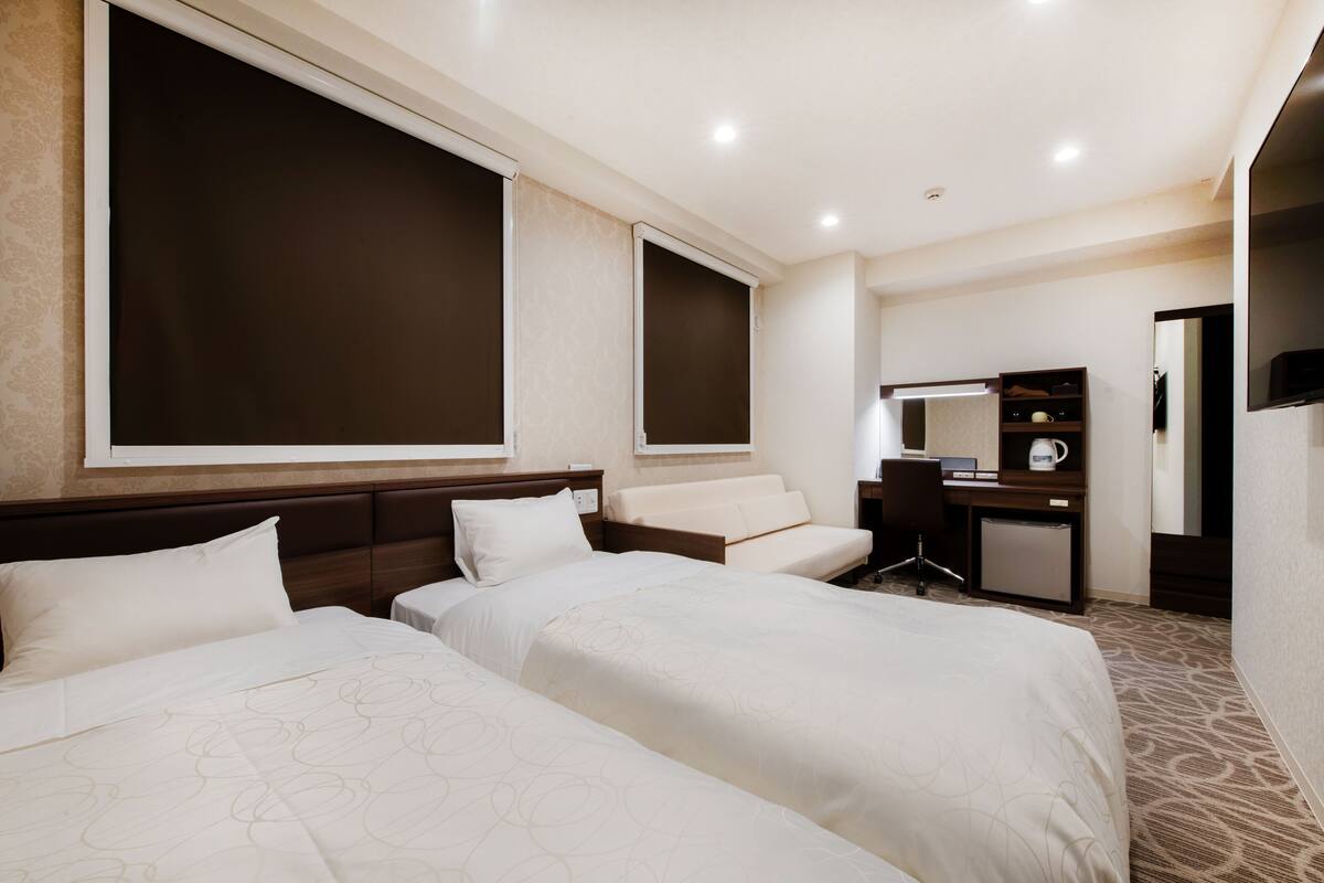A hotel room with two beds, a desk, a chair, a small refrigerator, and a large mirror.
