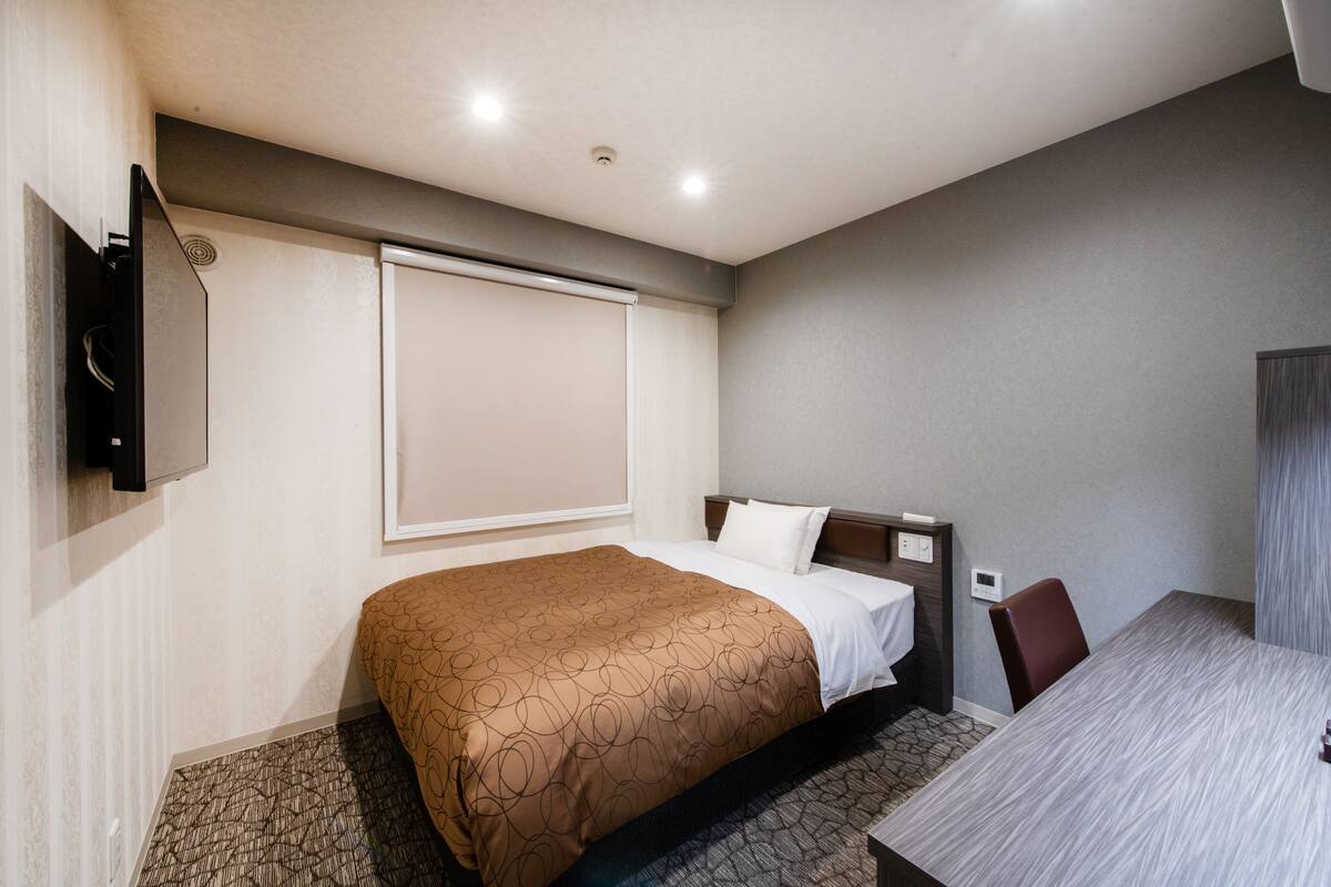 A hotel room with a bed, a desk, and a television.