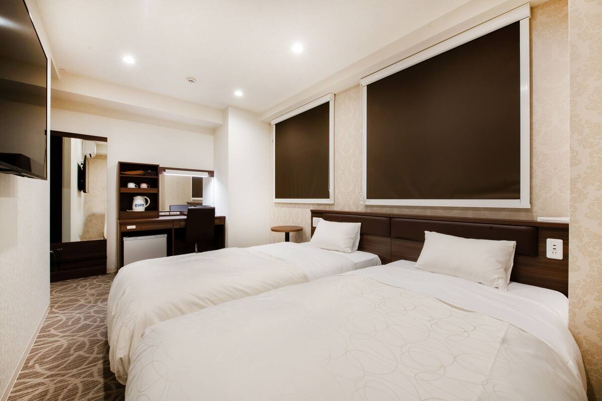 A hotel room with two beds, a desk, a mirror, and a large window.