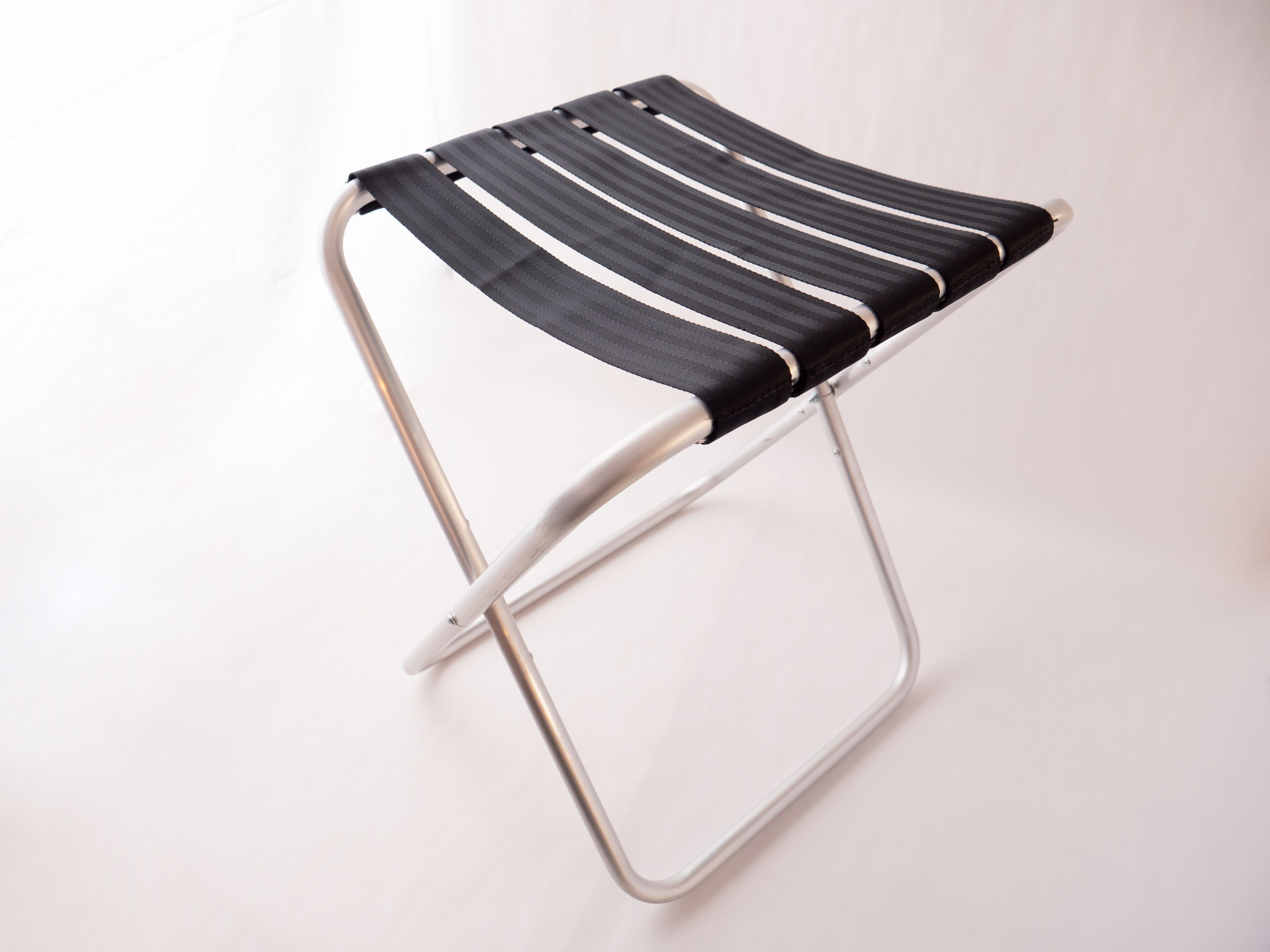 A modern, minimalist stool with a metal frame and black and white striped fabric seat.