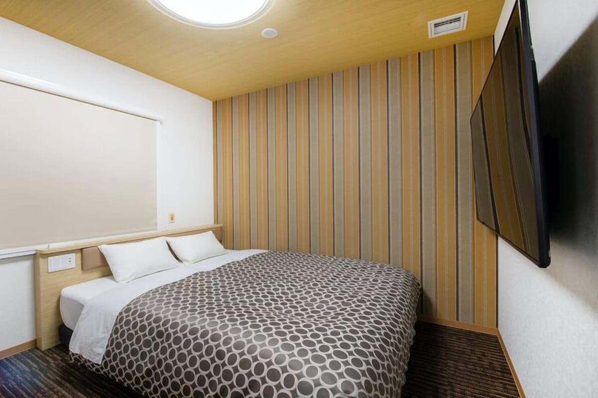 A hotel room with a bed, a large window, a wall-mounted TV, and a striped wallpaper design.
