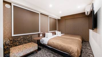 A hotel room with a large bed, a sofa, a small table, and a wall-mounted TV.