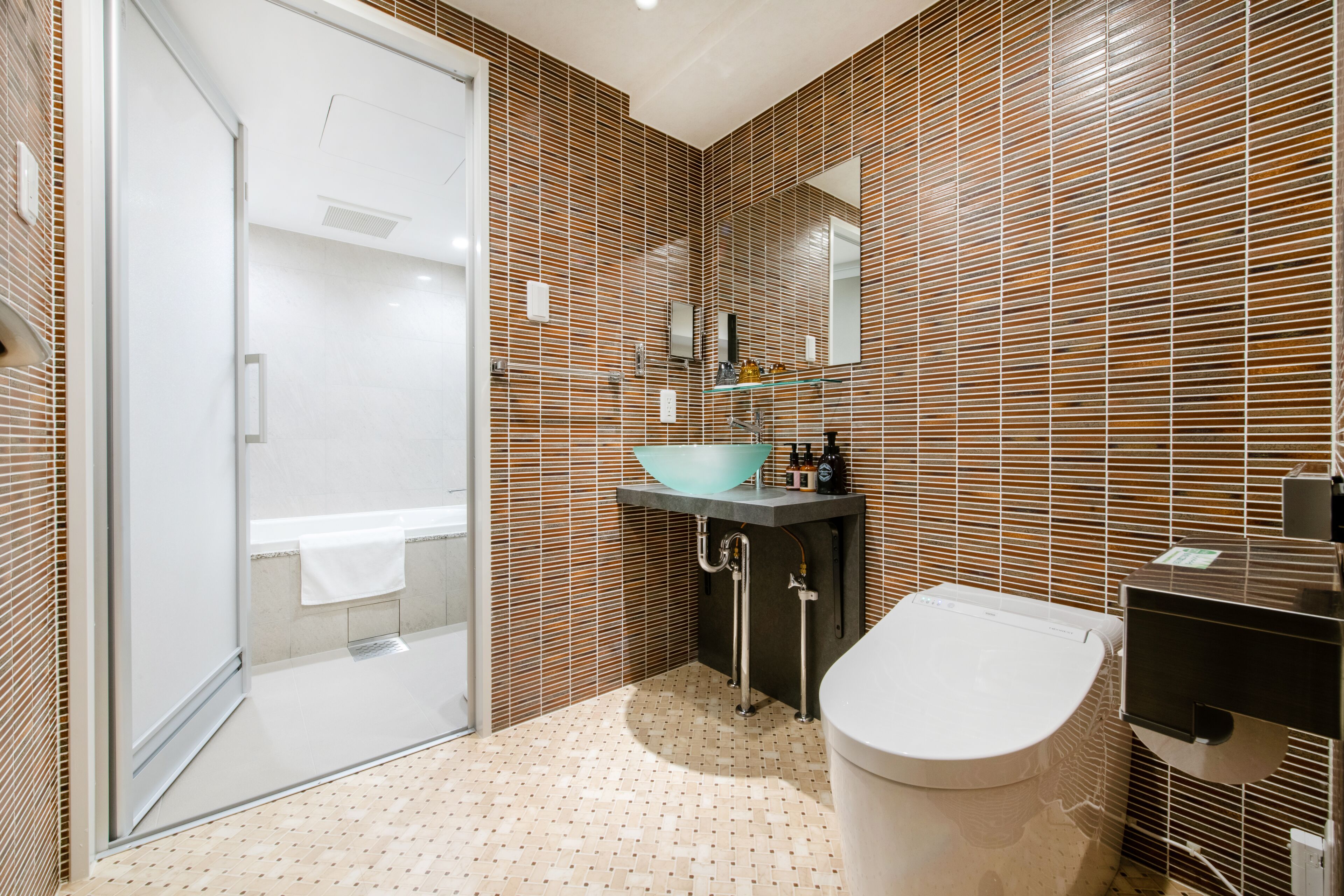A modern bathroom with a glass shower, a sink with a blue basin, and a toilet.