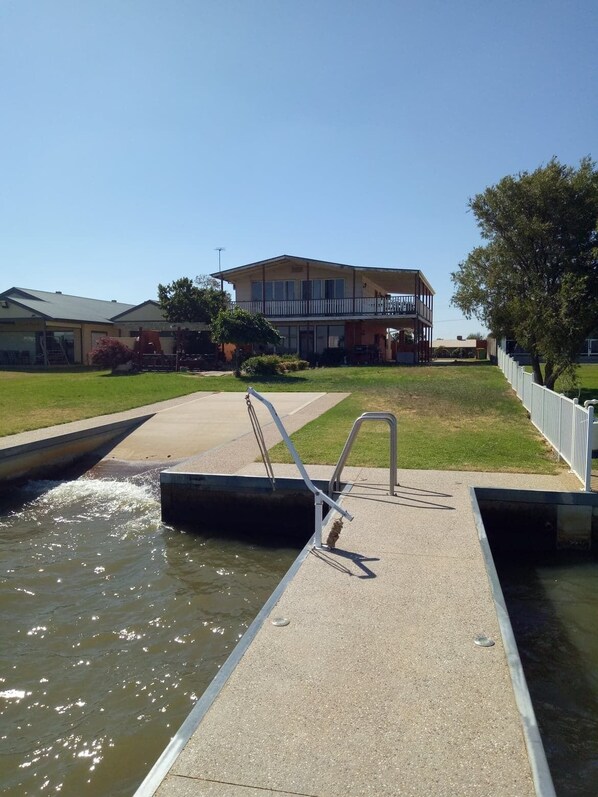 A building with a balcony, a pool with a ladder, and a grassy area.
