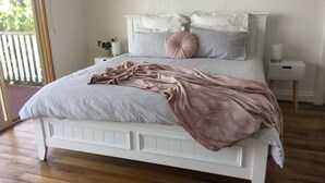 A bedroom with a white bed, a pink blanket, and a grey polka-dotted bedspread.