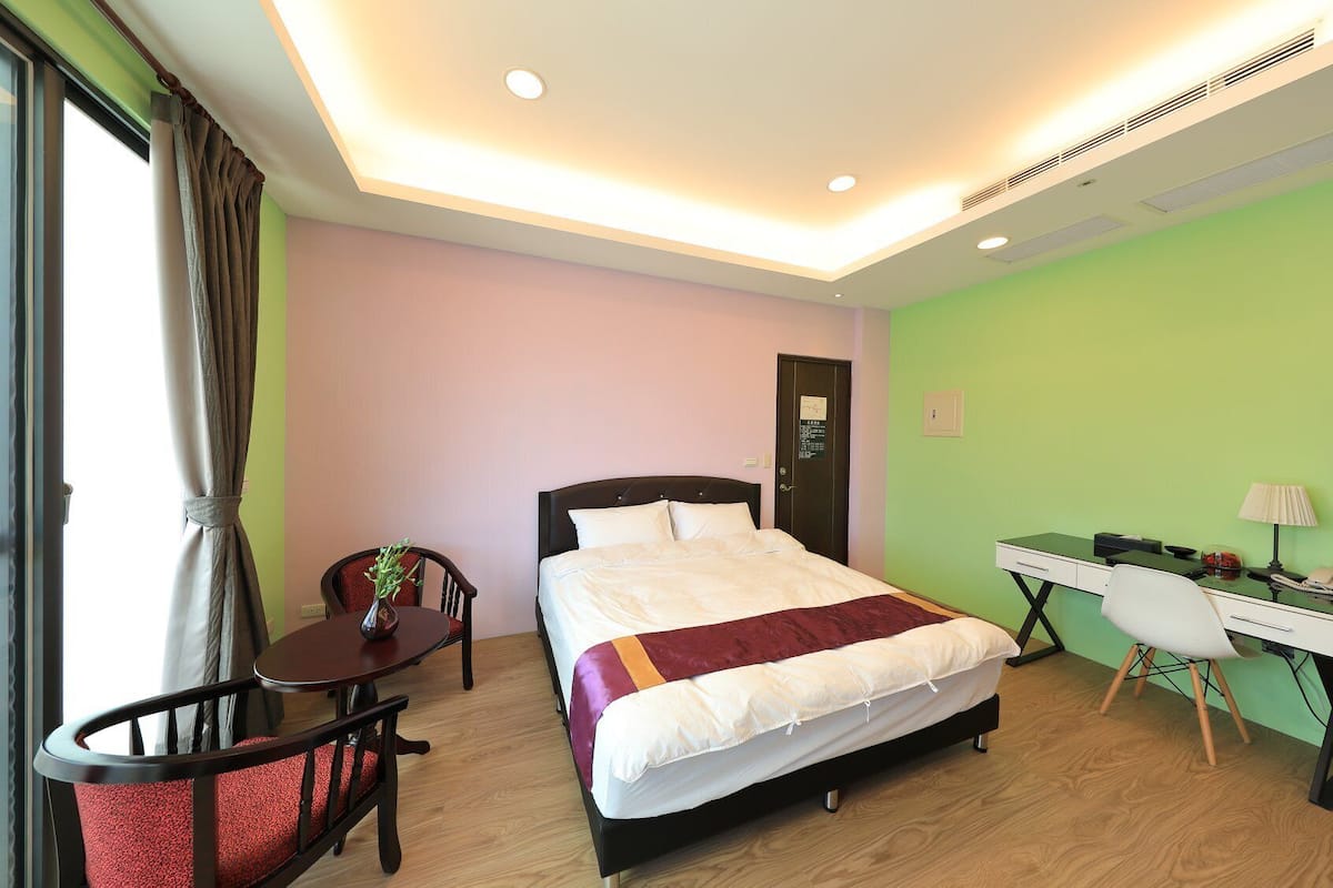 A hotel room with a bed, desk, chair, and a window with curtains.