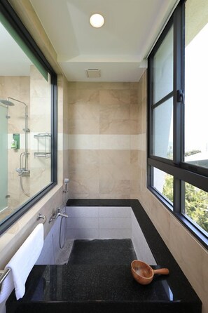 A modern bathroom with a black countertop, a wooden bowl, a glass shower enclosure, and a view through a large window.