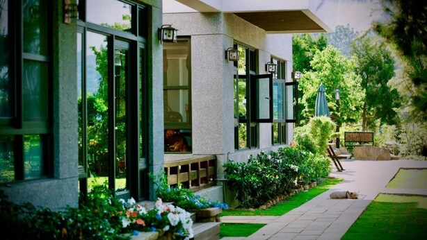 A modern building with large windows, a stone facade, and a well-maintained garden with a pathway and outdoor seating. - Five mountains and Three Water B&B (Shuili)