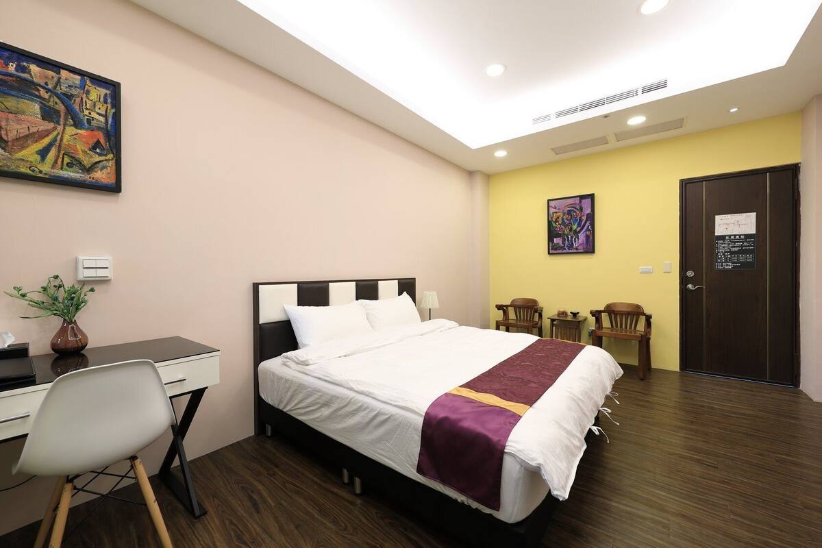 A hotel room with a bed, desk, chairs, and artwork on the walls.