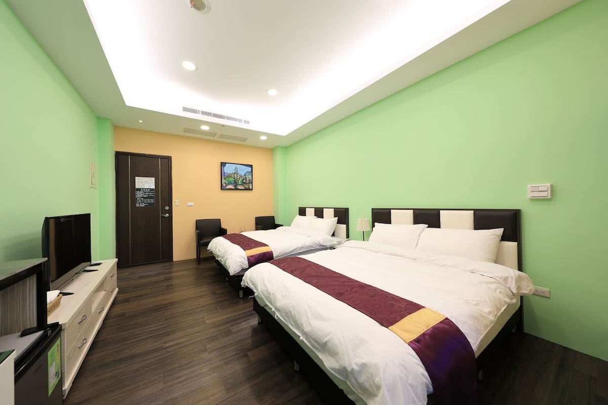 A hotel room with two beds, a TV, a desk, and a door.