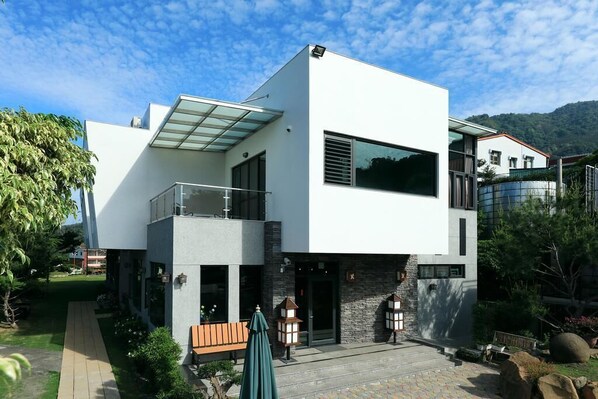 A modern two-story house with a balcony, large windows, and a stone facade.