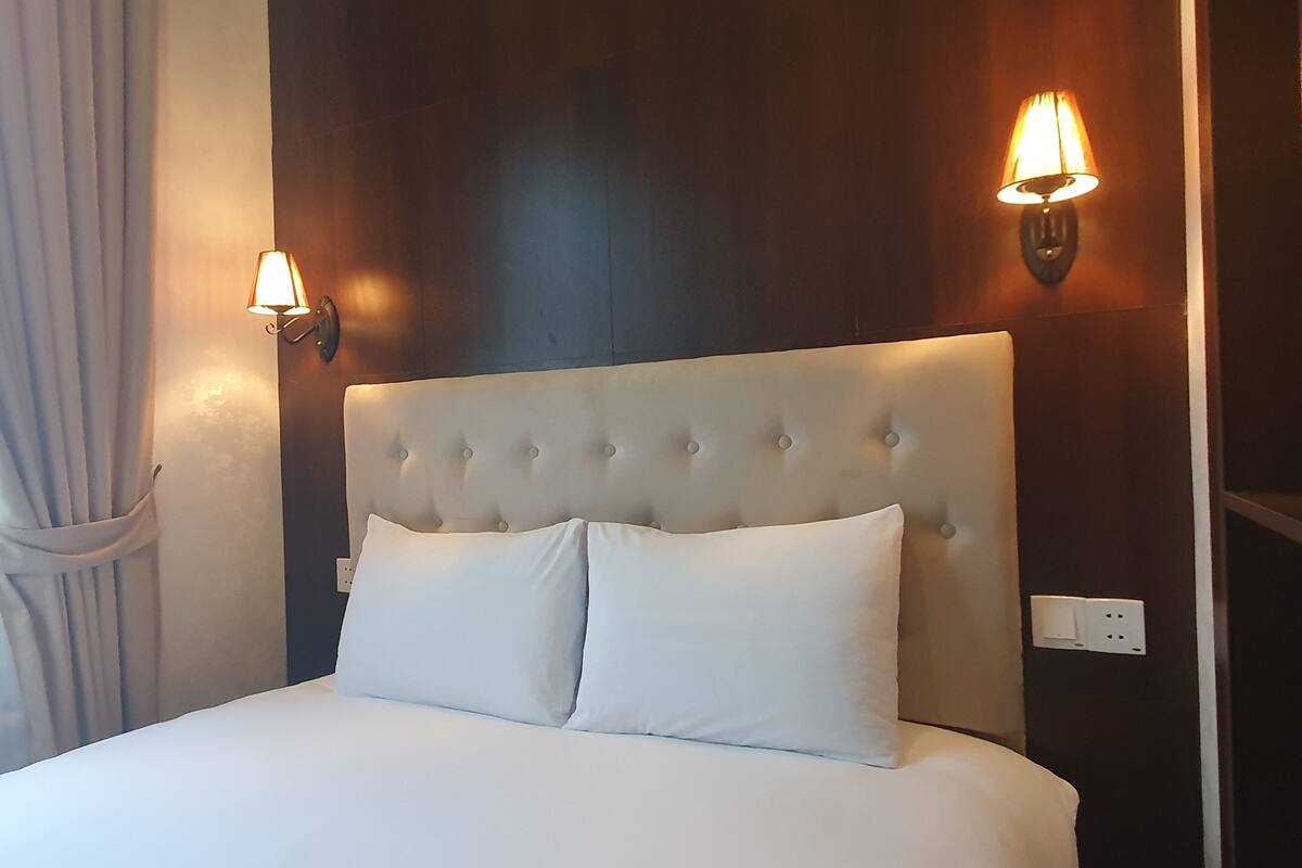 Un lit bien fait, doté d’une tête de lit capitonnée, de deux lampes fixées au mur et d’une prise de courant sur le mur.