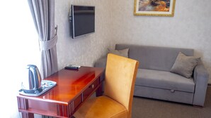 Ein Hotelzimmer mit einem Holztisch, einem grauen Sofa, einem Fernseher und einem Bild an der Wand.