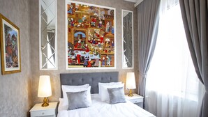 Ein Hotelzimmer mit einem großen Bett, zwei Nachttischen mit Lampen, einem großen gerahmten Kunstwerk über dem Bett und einem Fenster mit Vorhängen.
