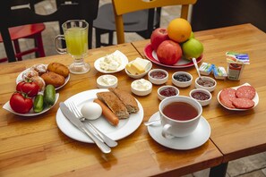 Une table dressée avec des aliments pour le petit-déjeuner, notamment du pain, des œufs, des saucisses, des fruits et des boissons.