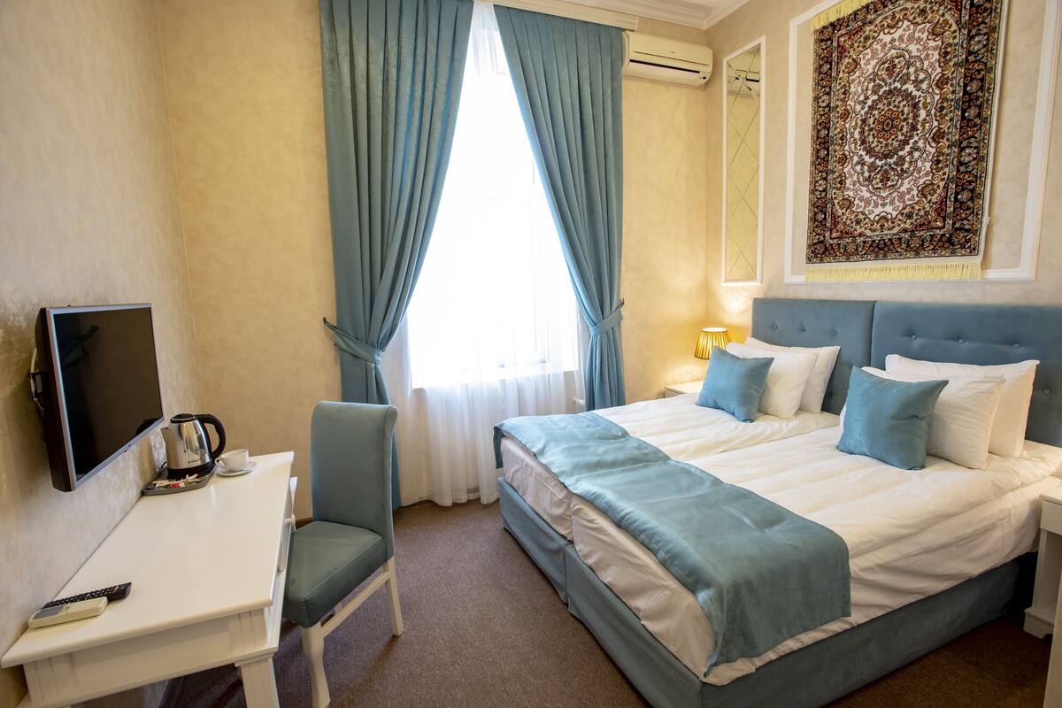 Une chambre d’hôtel équipée d’un lit, d’un bureau, d’une chaise, d’une télévision et d’une fenêtre avec des rideaux.