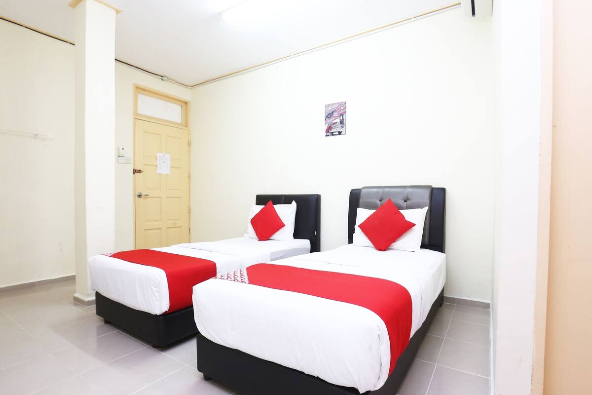 Habitación de hotel con dos camas, cada una con cabecero negro y almohadas rojas.
