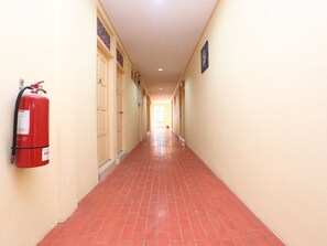 Un pasillo con un extintor a la izquierda, puertas a ambos lados y un cartel en la pared derecha.