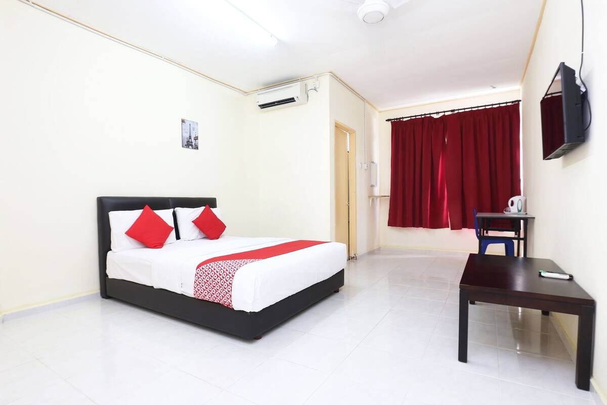 Habitación de hotel con cama, escritorio, silla, televisión y aire acondicionado.