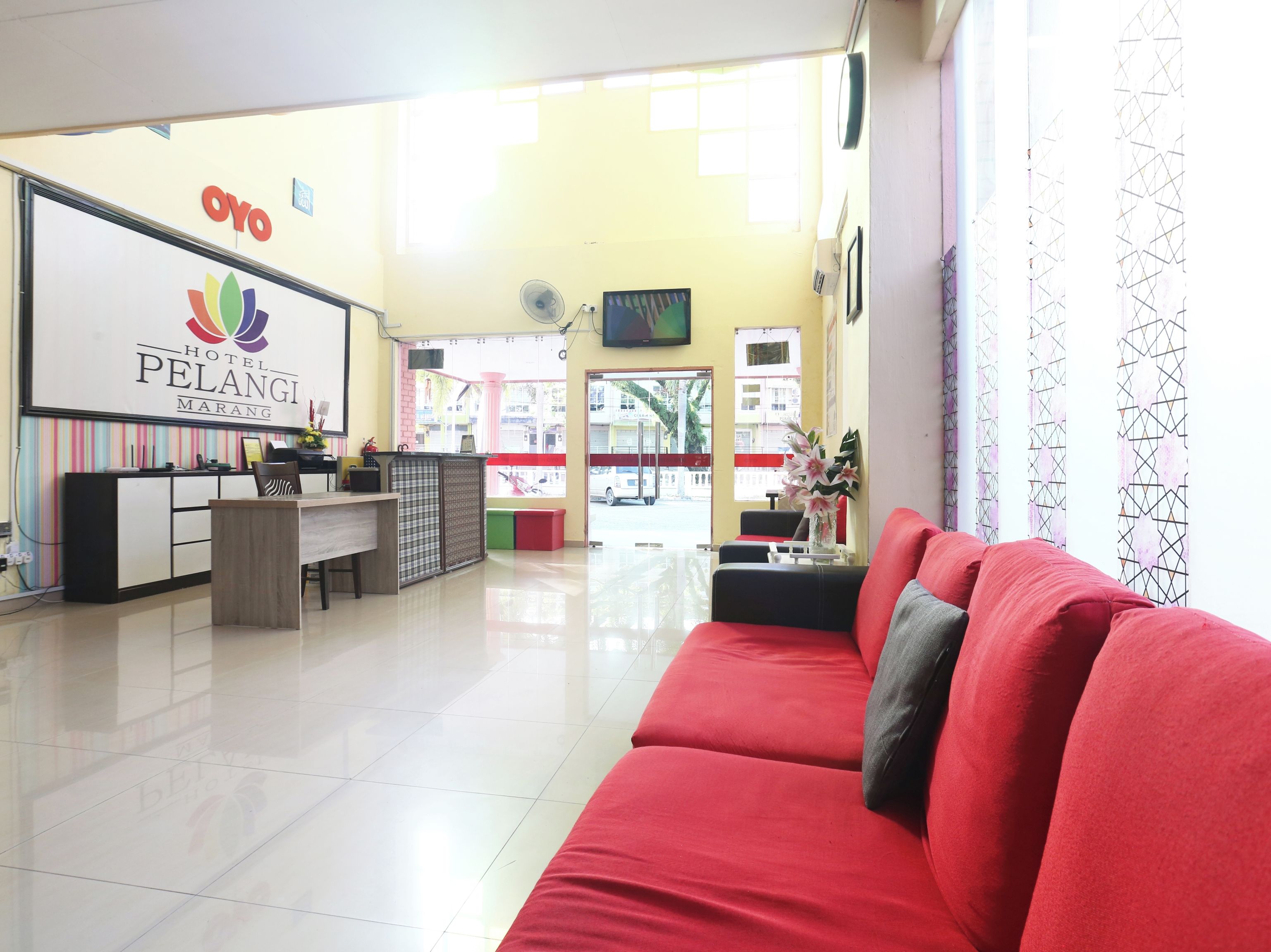 A hotel reception area with a reception desk, a red sofa, and a large window with a view of the street.