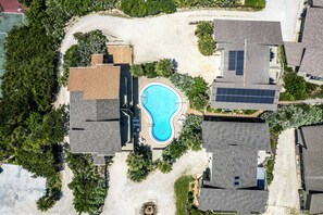 Vista aérea de uma área residencial com piscina, cercada por casas, painéis solares e árvores.