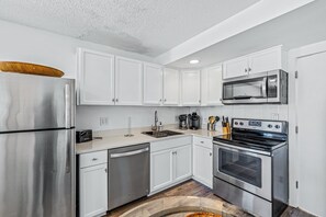 A modern kitchen with stainless steel appliances, white cabinetry, and a central island. - Renovated Sea Dunes 2BR with Ocean View Ground Level and Pool Next Door (New Smyrna Beach)
