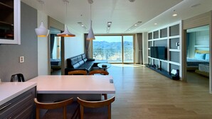 Une chambre d’hôtel moderne dotée d’un coin repas, d’un canapé, d’une télévision et d’un balcon offrant une vue sur la montagne.