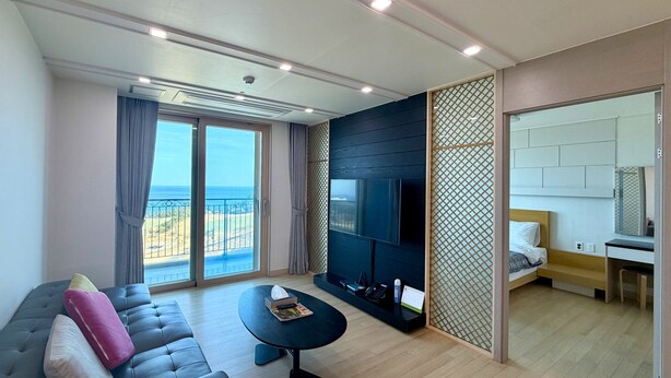 Un salon moderne avec un canapé, une table basse, un téléviseur et un balcon offrant une vue sur la mer.