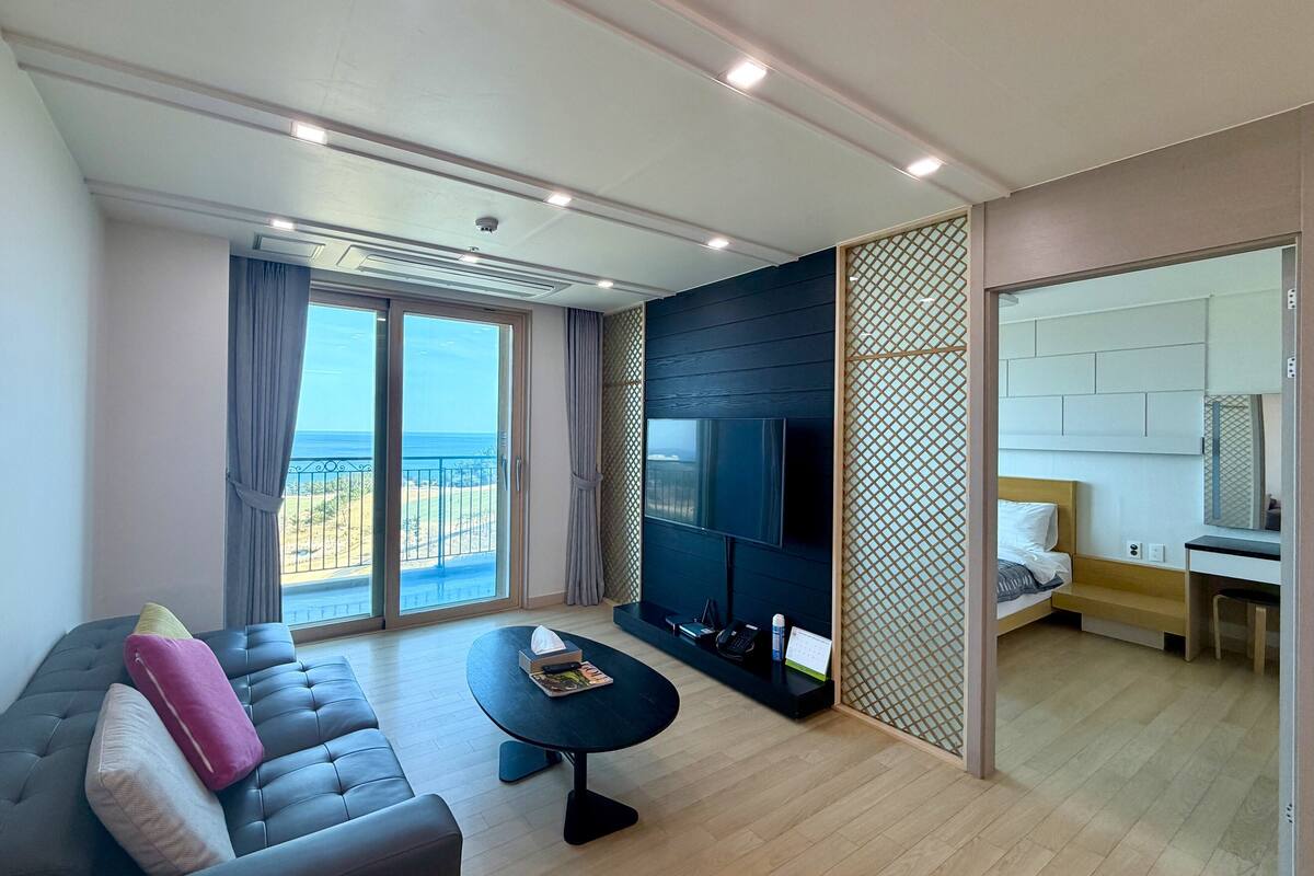 Een moderne woonkamer met een bank, een salontafel, een televisie en een balkon met uitzicht op zee.
