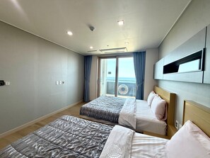 Una habitación de hotel moderna con dos camas, un ventanal con cortinas, un televisor montado en el techo y un balcón con vistas circulares al mar.