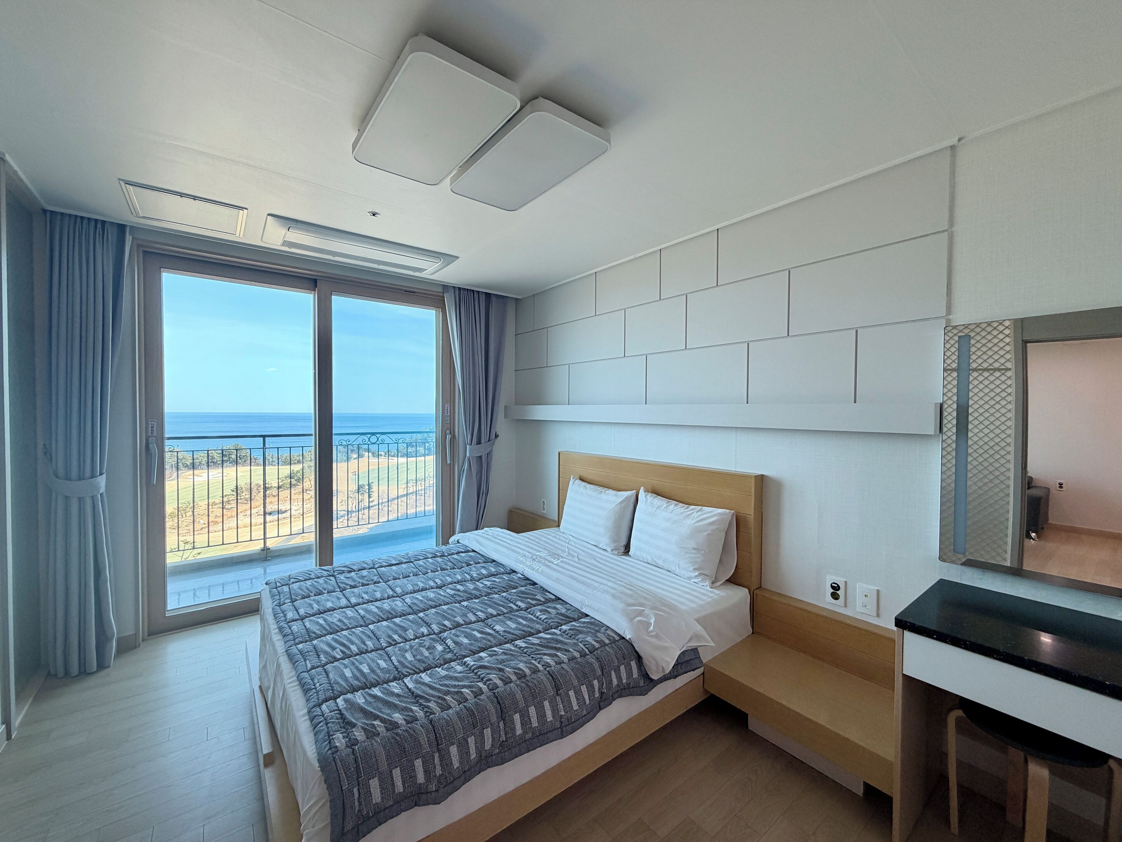 A modern hotel room with a large bed, a desk, and a view of the ocean.